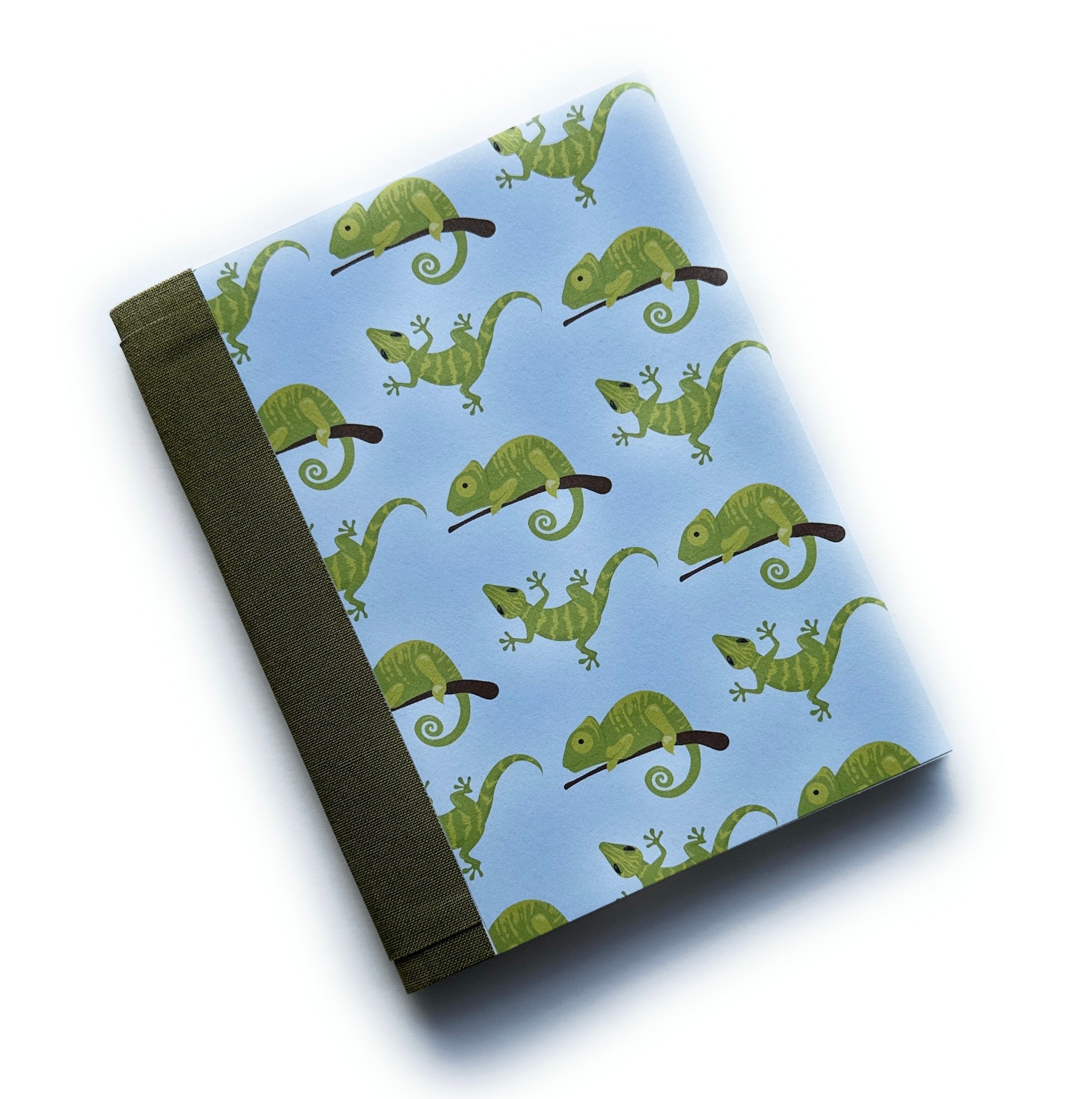 The Chilling Chameleon DIY Bookmaking Kit features a whimsical design with green chameleons perched on branches against a soft blue background. Paired with a deep green book cloth spine, this fun and creative bookbinding kit includes all the materials needed to craft a personalized journal. Ideal for nature lovers, reptile enthusiasts, and anyone who enjoys unique, handmade stationery.