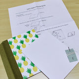 A DIY bookmaking kit featuring a handcrafted pocket journal with a charming yellow pineapple cover and an olive green book cloth spine. The kit includes step-by-step illustrated instructions, sewing thread, a needle, and premium blank paper, making it perfect for beginners and craft enthusiasts who want to create their own personalized booklet.
