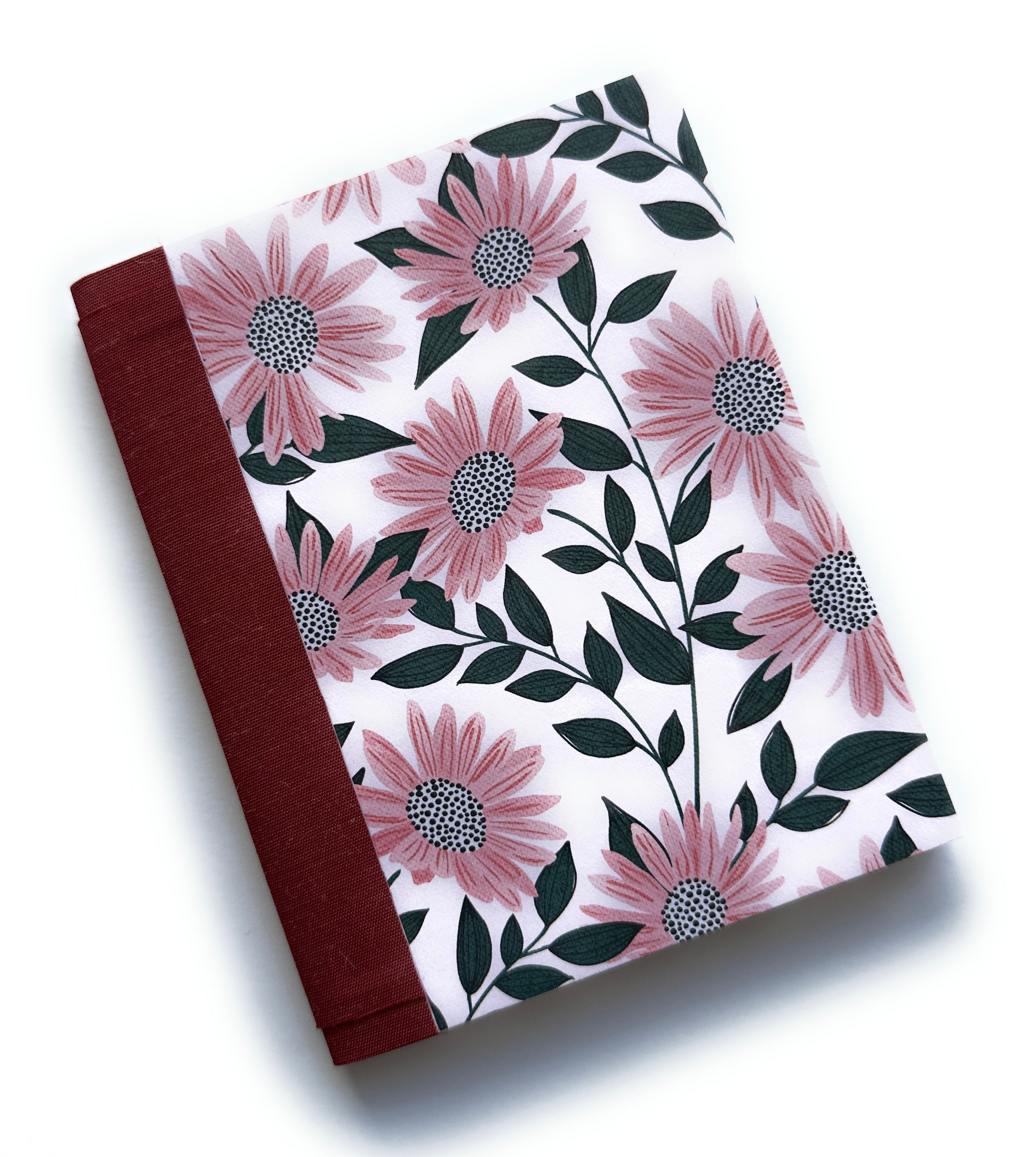 The Daisy Dreams DIY Bookmaking Kit features a beautifully handcrafted cover adorned with soft pink daisies and deep green leaves on a light background. Complemented by a rich burgundy book cloth spine, this elegant DIY kit provides all the materials needed to create a personalized handmade book. Ideal for journal enthusiasts, writers, and craft lovers, this bookbinding kit offers a unique and creative way to make a custom floral-themed notebook.