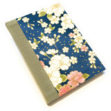 A beautifully handcrafted hardcover journal featuring a Japanese sakura (cherry blossom) fabric design with gold accents on a rich navy blue background. This artisan notebook is bound with Japanese book cloth for durability and elegance. Perfect for writing, journaling, sketching, or gift-giving, this floral-themed notebook blends traditional craftsmanship with timeless beauty, making it an ideal keepsake for creatives and stationery lovers.