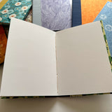 An open handmade keepsake card showcasing high-quality textured blank pages, ideal for heartfelt messages, signatures, or special notes. The fabric-covered hardcover adds elegance, while the surrounding designs highlight the variety of available styles.