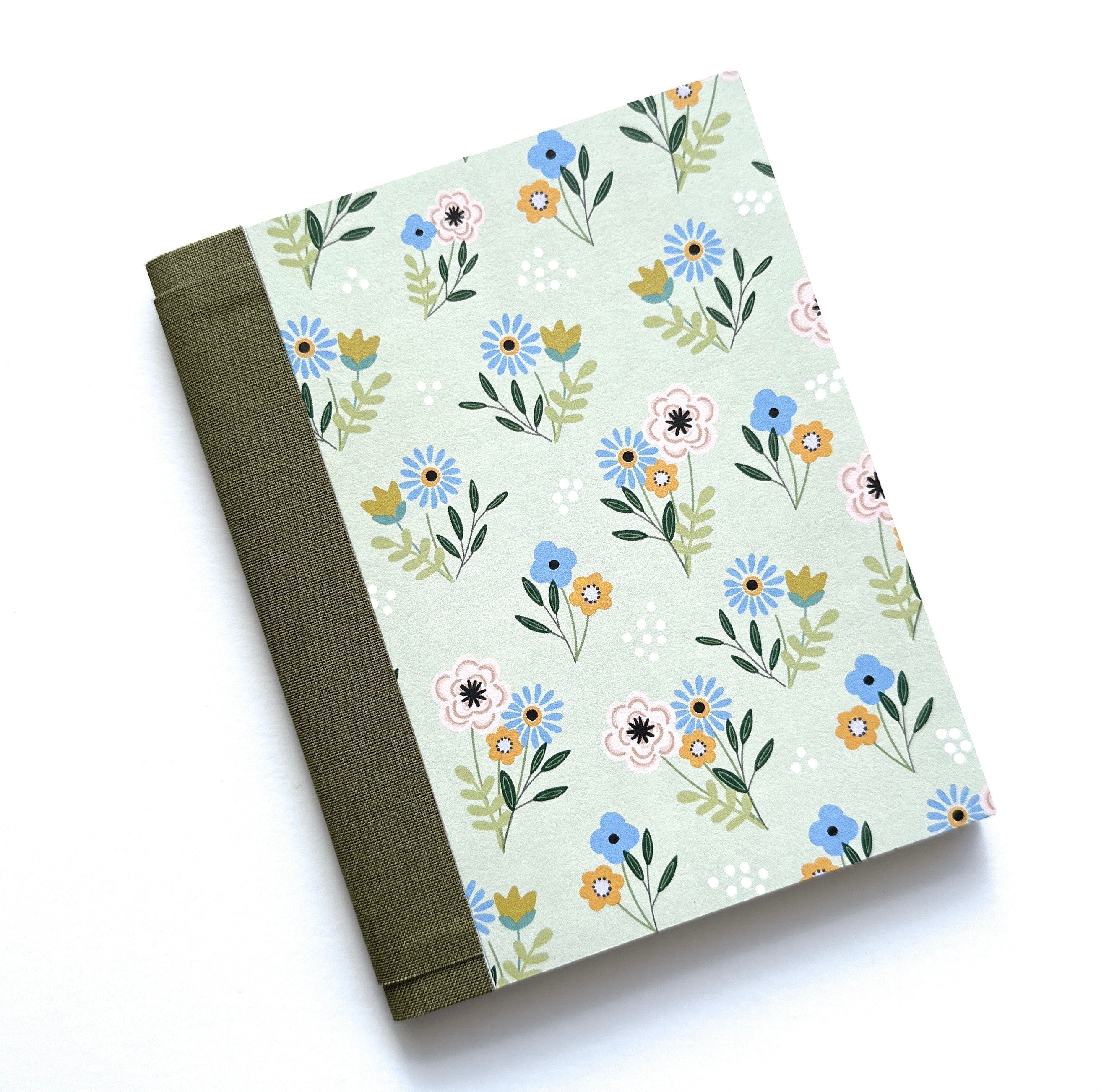 The Pastel Blooms DIY Bookmaking Kit features a charming floral design with delicate pastel-colored flowers in soft blue, peach, and cream, set against a pale green background. The journal is bound with a deep green book cloth spine, giving it an elegant and timeless look. This DIY kit includes all the materials needed to create a handmade booklet, making it a perfect craft for journal lovers, writers, and creative enthusiasts who enjoy artisan stationery and floral-inspired designs.
