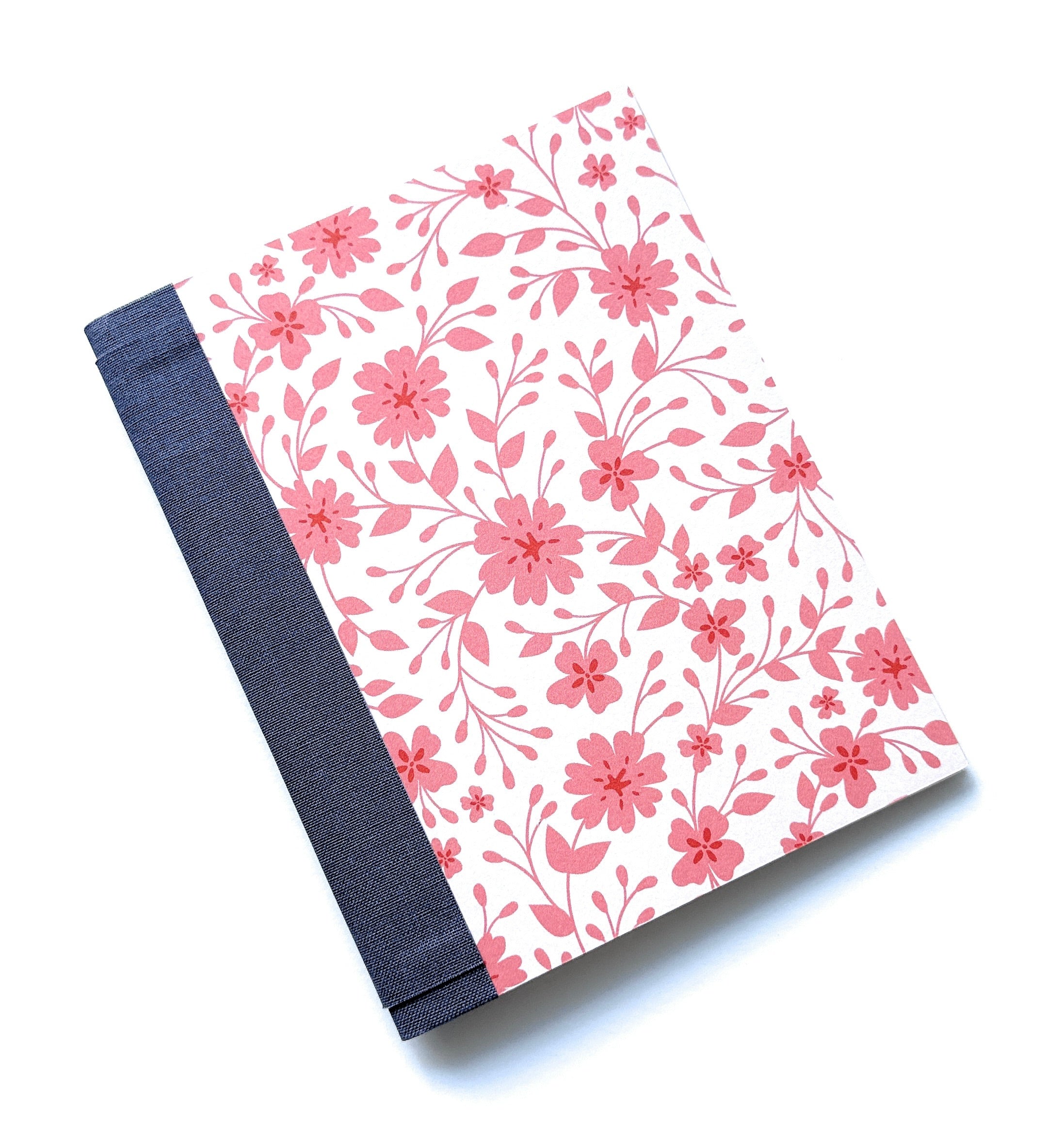 The Pink Blossom DIY Bookmaking Kit features a delicate pink floral pattern on a crisp white background, complemented by a deep blue book spine. This handmade bookbinding kit includes all the essentials to create a beautifully crafted journal, ideal for writers, artists, and stationery enthusiasts who love elegant floral aesthetics.