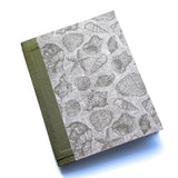 The Seaside Stories DIY Bookmaking Kit features a handcrafted book cover with intricate gray illustrations of seashells, starfish, and ocean treasures on a textured background. Complemented by an earthy green book cloth spine, this ocean-inspired DIY bookbinding kit provides everything needed to create a personalized handmade journal. Perfect for beach lovers, writers, and creatives looking to craft a unique keepsake for their thoughts and memories.