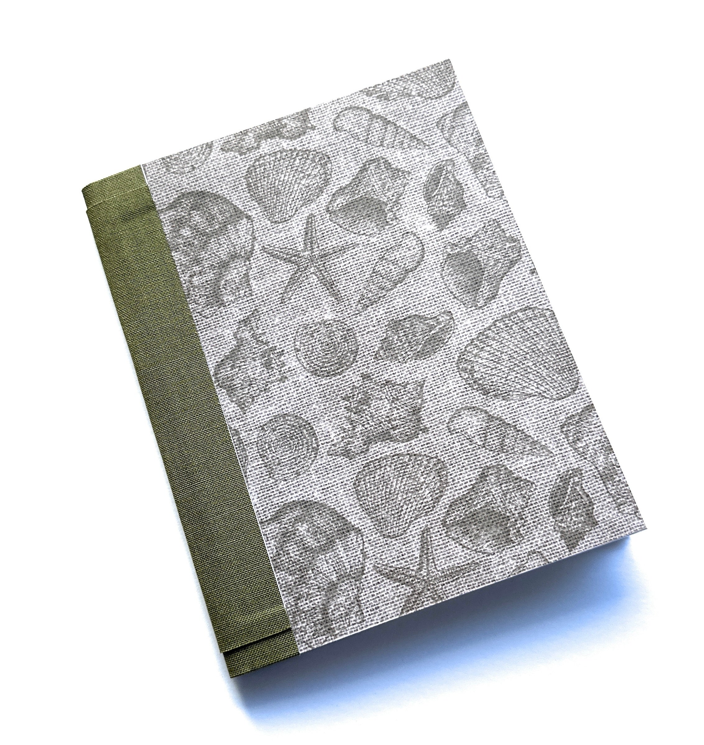 The Seaside Stories DIY Bookmaking Kit features a handcrafted book cover with intricate gray illustrations of seashells, starfish, and ocean treasures on a textured background. Complemented by an earthy green book cloth spine, this ocean-inspired DIY bookbinding kit provides everything needed to create a personalized handmade journal. Perfect for beach lovers, writers, and creatives looking to craft a unique keepsake for their thoughts and memories.