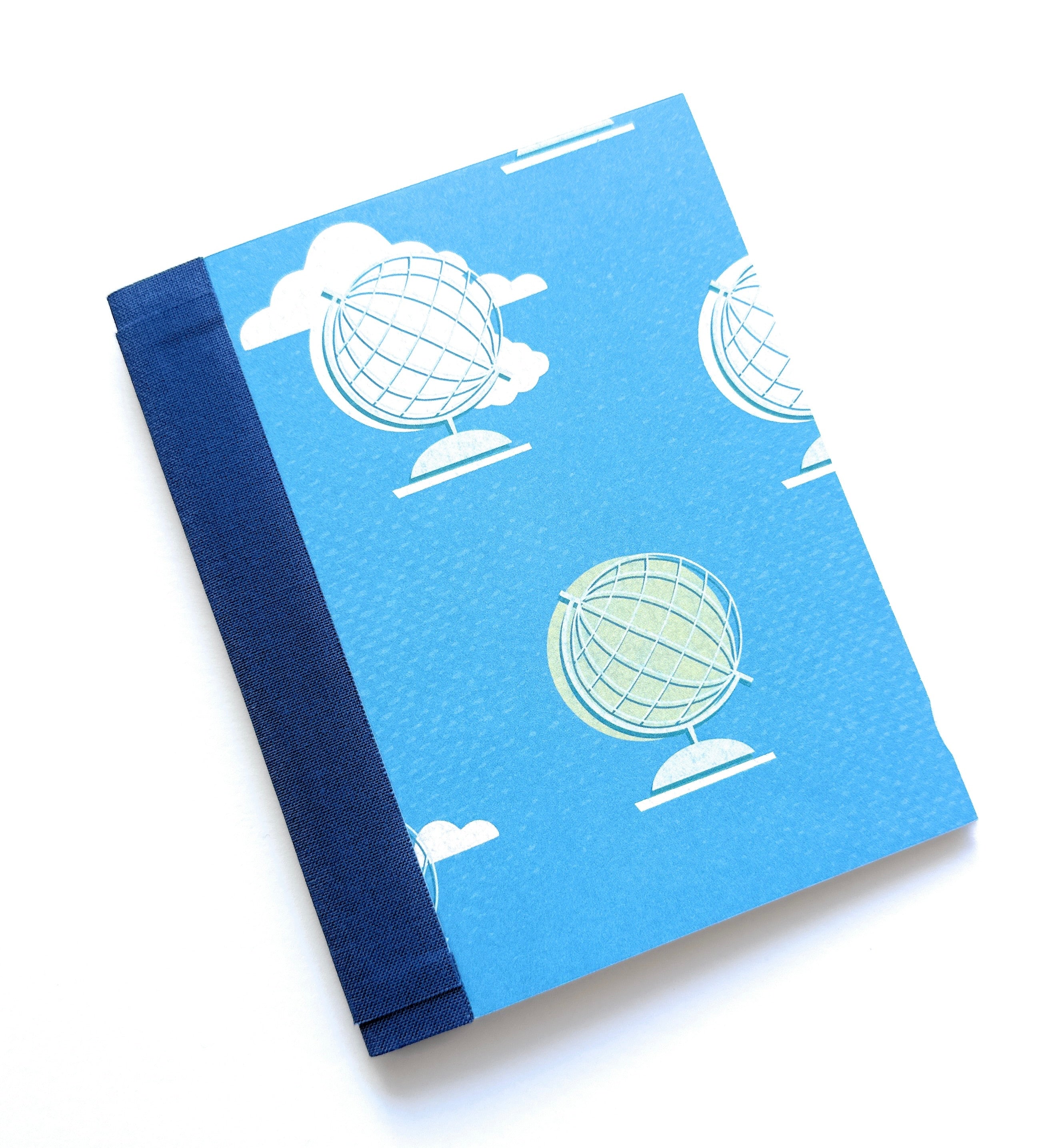 The World Awaits DIY Bookmaking Kit features a vibrant blue cover adorned with illustrated globes and fluffy white clouds, evoking a sense of adventure and exploration. Bound with a deep navy blue book cloth spine, this handmade journal kit is perfect for travelers, writers, and creatives looking to document their journeys or dreams. The kit includes all the materials needed to craft a personalized booklet, making it an ideal project for bookbinding enthusiasts and those who love unique, travel-themed stati