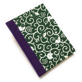 This handcrafted journal features a deep green fabric cover adorned with playful cat illustrations and swirling patterns. Bound with a purple bookbinding cloth, it is perfect for journaling, sketching, or note-taking, making it a great gift for cat lovers.