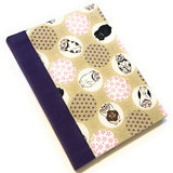 This image shows a handmade book with a beige fabric cover featuring a whimsical design. The cover is adorned with various circular patterns, each containing playful illustrations of cats in different poses. Some circles have floral patterns in pink and brown. The spine is covered with a deep purple fabric, providing a bold contrast to the lighter, playful cover design. The book is expertly crafted, demonstrating a clean and polished finish.