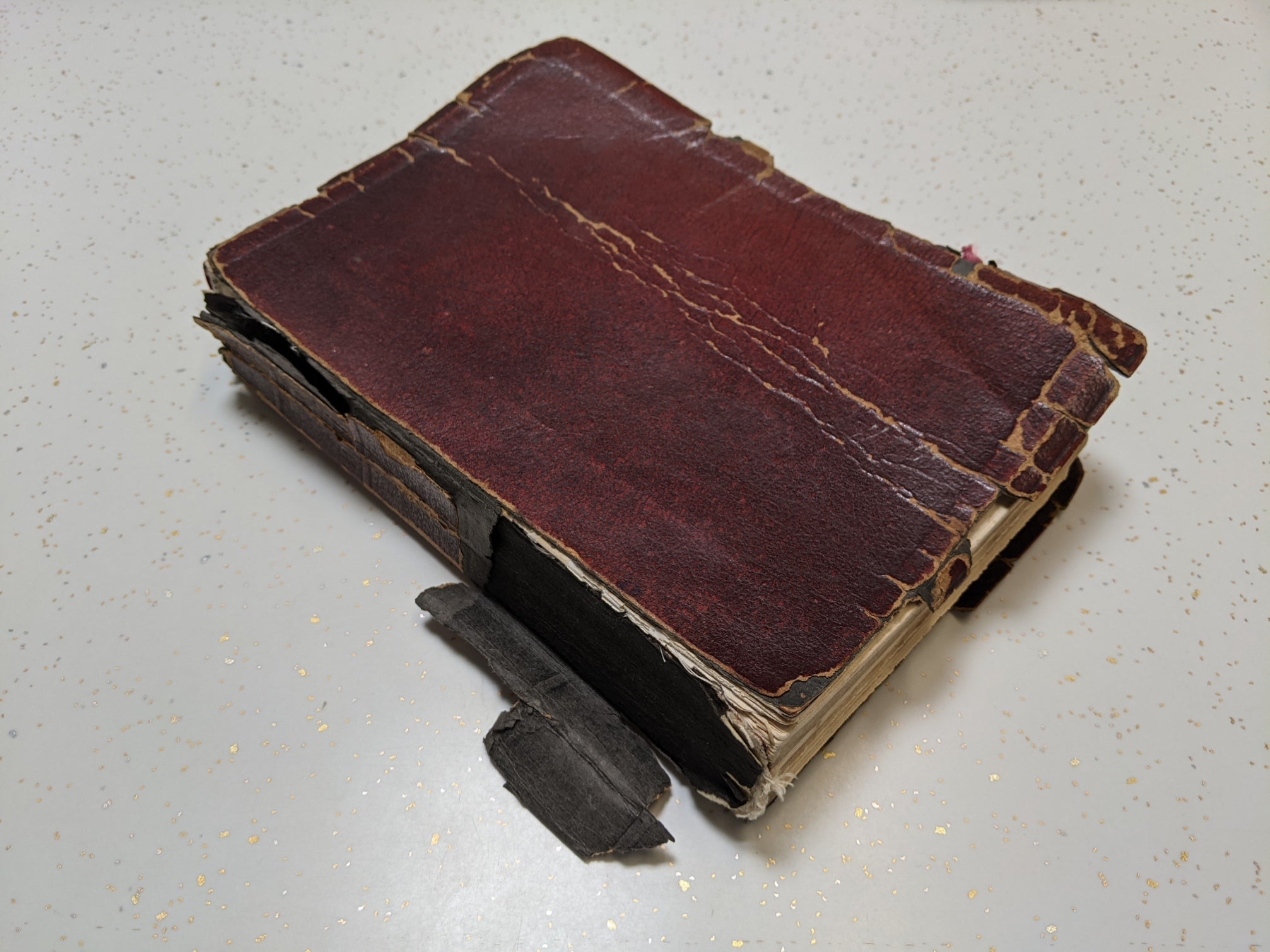 This image showcases an antique book in a deteriorated state before restoration, with its cracked and peeling red leather cover, detached spine, and fragile binding. A prime example of book conservation needs, this "before" photo highlights the effects of time and wear, setting the stage for an expert restoration to preserve its historical and sentimental value.