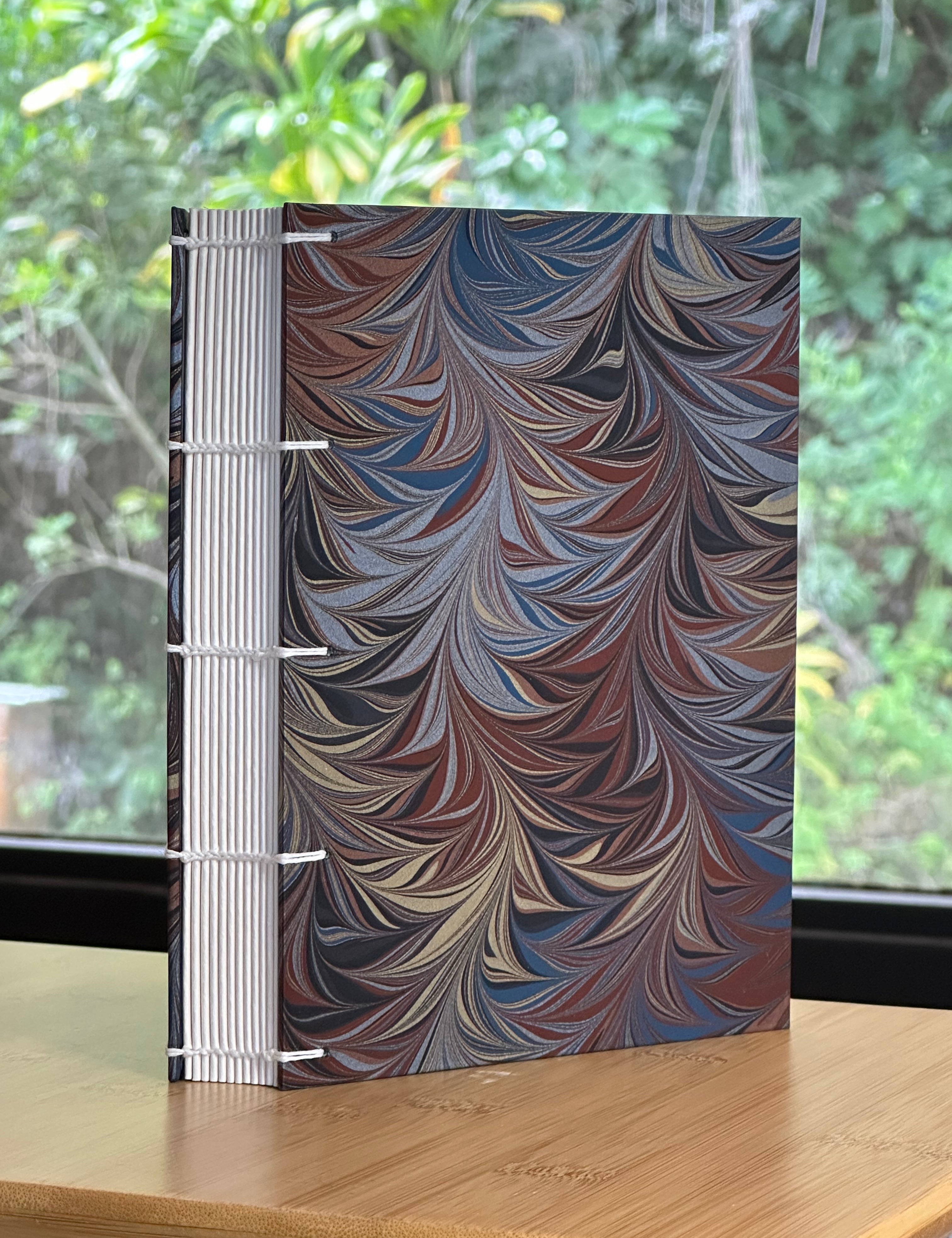 Coptic Style Bound journal with a Renato Crepaldi marbled cover on a wooden surface with a blurred green background