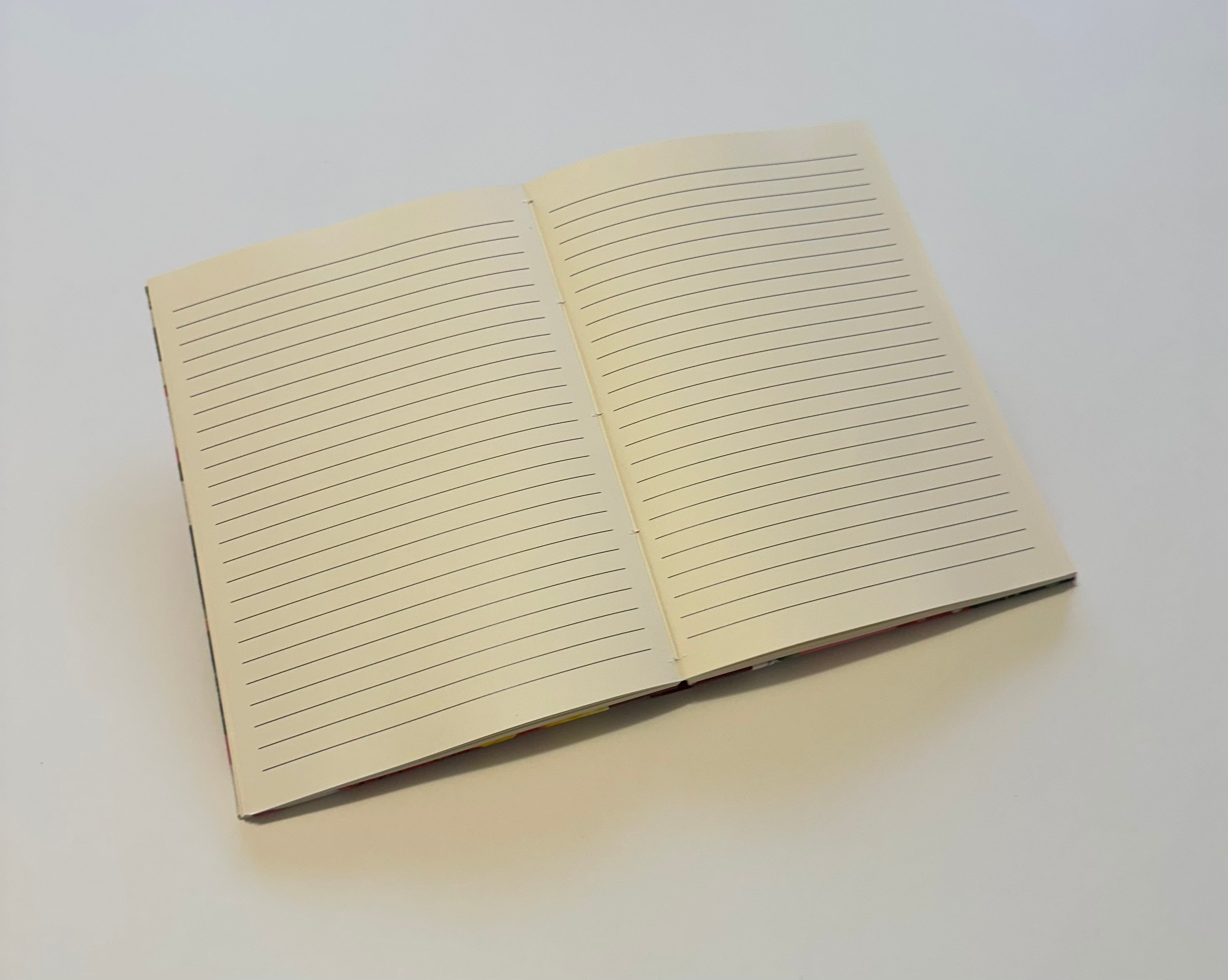 An open journal with cream-colored lined pages lies on a clean, white surface. The journal pages are blank, awaiting written content. The simple and elegant design of the journal highlights its usability for note-taking, journaling, or creative writing. The soft lines on the pages provide a guide for neat handwriting.