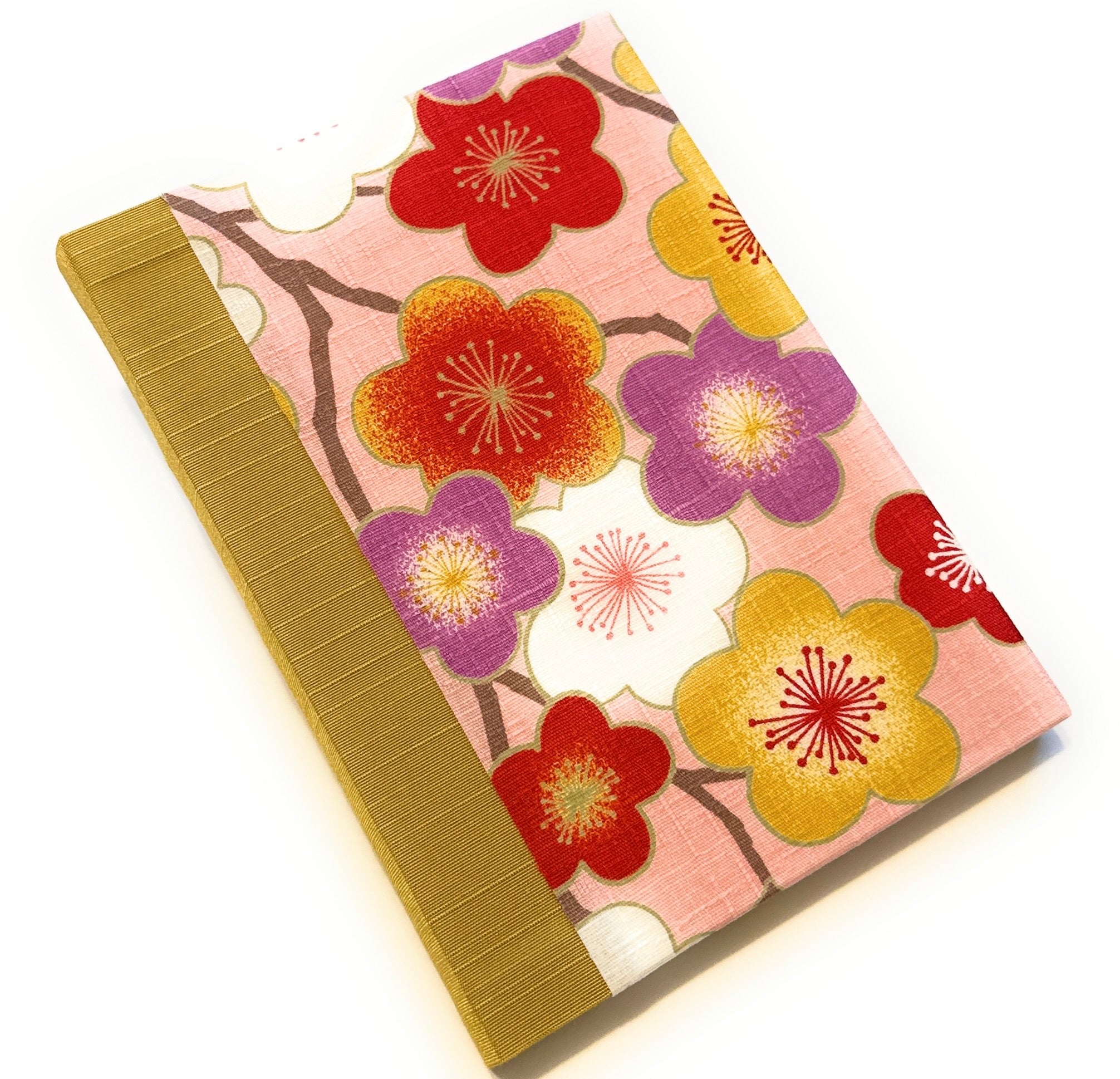 This image shows a handmade book with a pink fabric cover featuring a vibrant floral design. The cover is adorned with large flowers in red, purple, white, and yellow, each with detailed centers. The flowers are connected by brown branches, creating a lively and colorful pattern. The spine is covered with a yellow gold fabric, which complements the warm tones of the cover design. The book is meticulously crafted, showcasing a clean and professional finish.