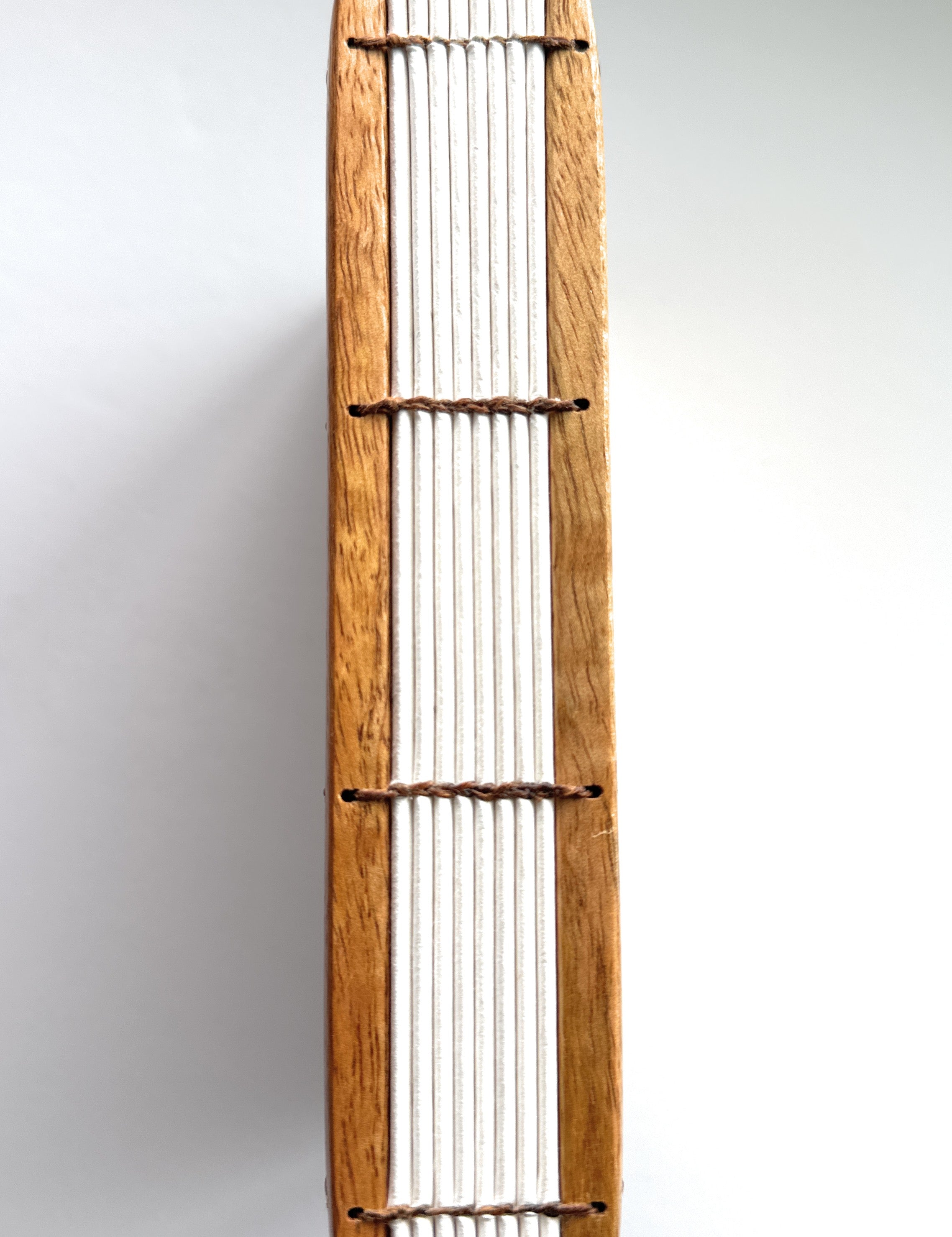 A close-up view of the Mango Wood Coptic Journal, showcasing its exposed spine.  The sturdy wooden covers are paired with durable thread stitching, allowing the journal to lay flat when open. This unique handmade book is perfect for journaling, sketching, or creative writing enthusiasts who appreciate craftsmanship and longevity.
