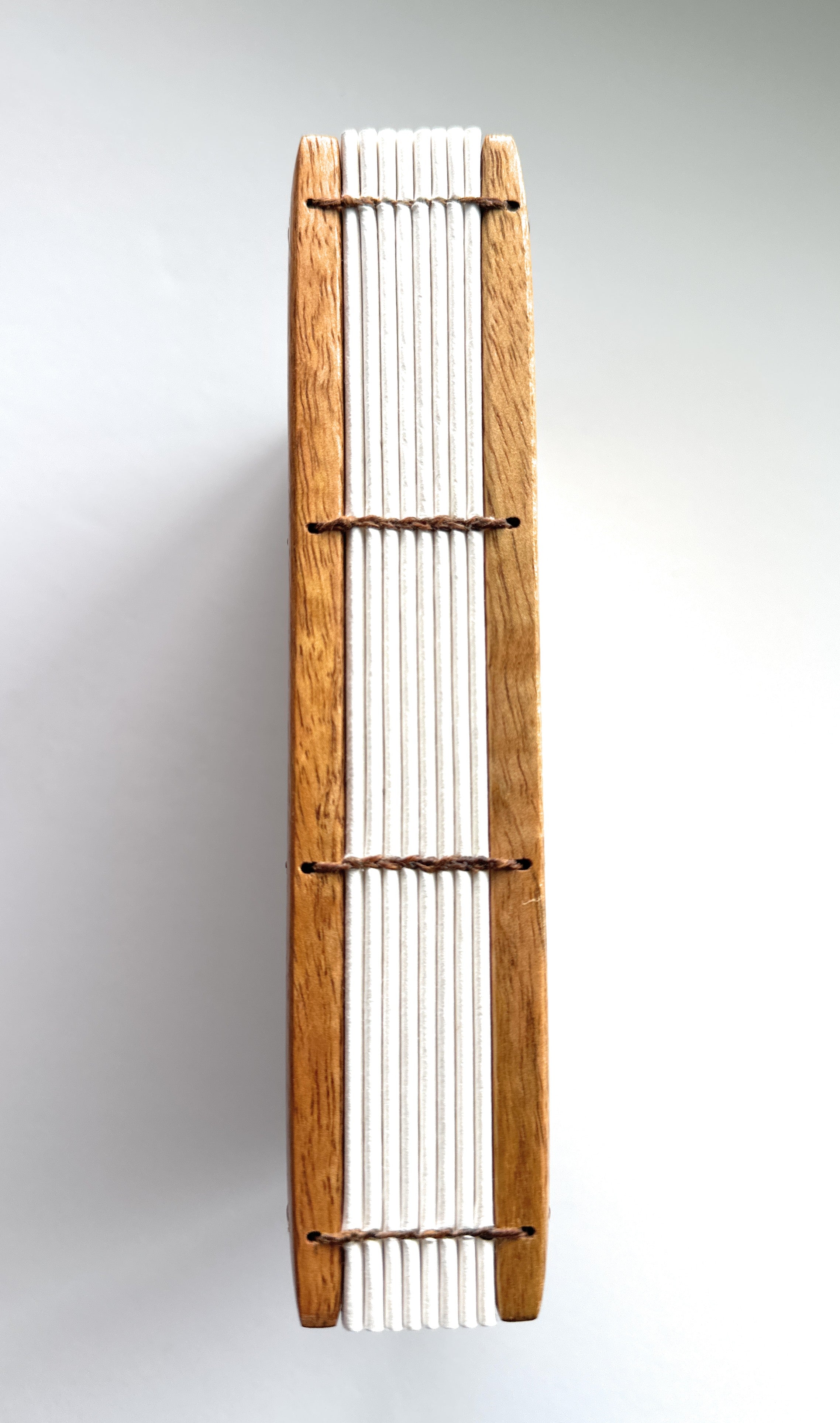 A close-up view of the Mango Wood Coptic Journal, showcasing its exposed spine.  The sturdy wooden covers are paired with durable thread stitching, allowing the journal to lay flat when open. This unique handmade book is perfect for journaling, sketching, or creative writing enthusiasts who appreciate craftsmanship and longevity.