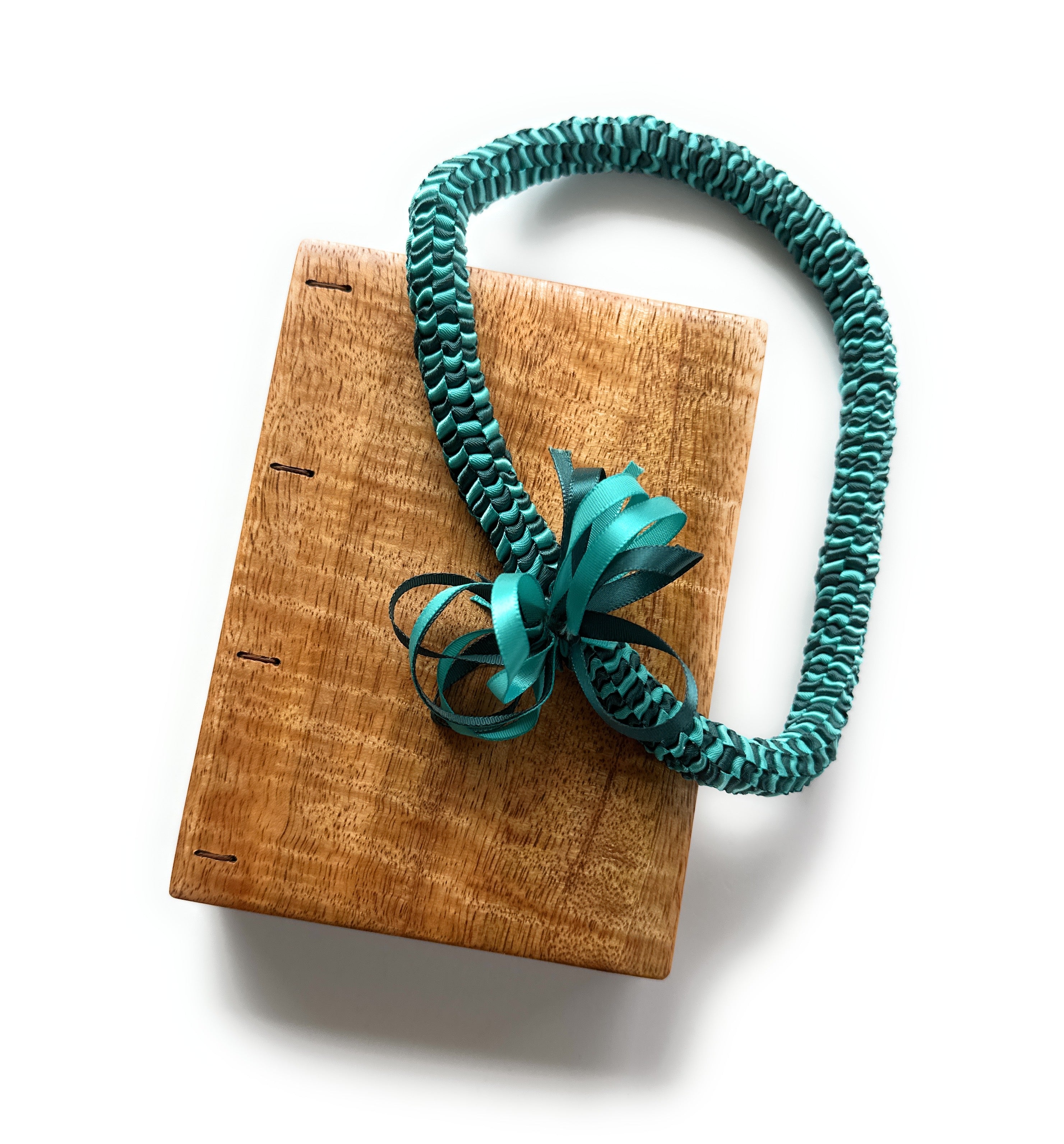A beautifully handcrafted Mango Wood Coptic Journal paired with a Hawaiian ribbon lei in teal. This elegant wooden notebook features an exposed spine for flexibility and durability, perfect for journaling, sketching, or gift-giving. The ribbon lei adds a touch of cultural significance, symbolizing love, friendship, and celebration. 