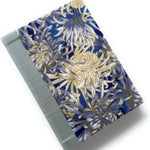 This handcrafted fabric journal showcases an elegant blue and gold chrysanthemum design, accented with a sturdy blue gray book cloth spine. The intricate floral pattern makes this notebook perfect for journaling, sketching, or creative writing. A beautifully crafted gift for writers, artists, and stationery lovers, this Japanese-inspired journal combines functionality with timeless artistry.
