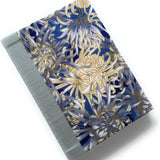 This handcrafted fabric journal showcases an elegant blue and gold chrysanthemum design, accented with a sturdy blue gray book cloth spine. The intricate floral pattern makes this notebook perfect for journaling, sketching, or creative writing. A beautifully crafted gift for writers, artists, and stationery lovers, this Japanese-inspired journal combines functionality with timeless artistry.