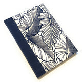 This handmade journal showcases a striking navy blue and white botanical leaf pattern on a high-quality fabric cover. The deep navy bookcloth spine complements the intricate tropical leaf design, creating a sophisticated yet nature-inspired look. Designed for writing, journaling, or sketching, this artisan notebook is crafted with durable materials, making it a perfect gift for writers, artists, and stationery lovers.