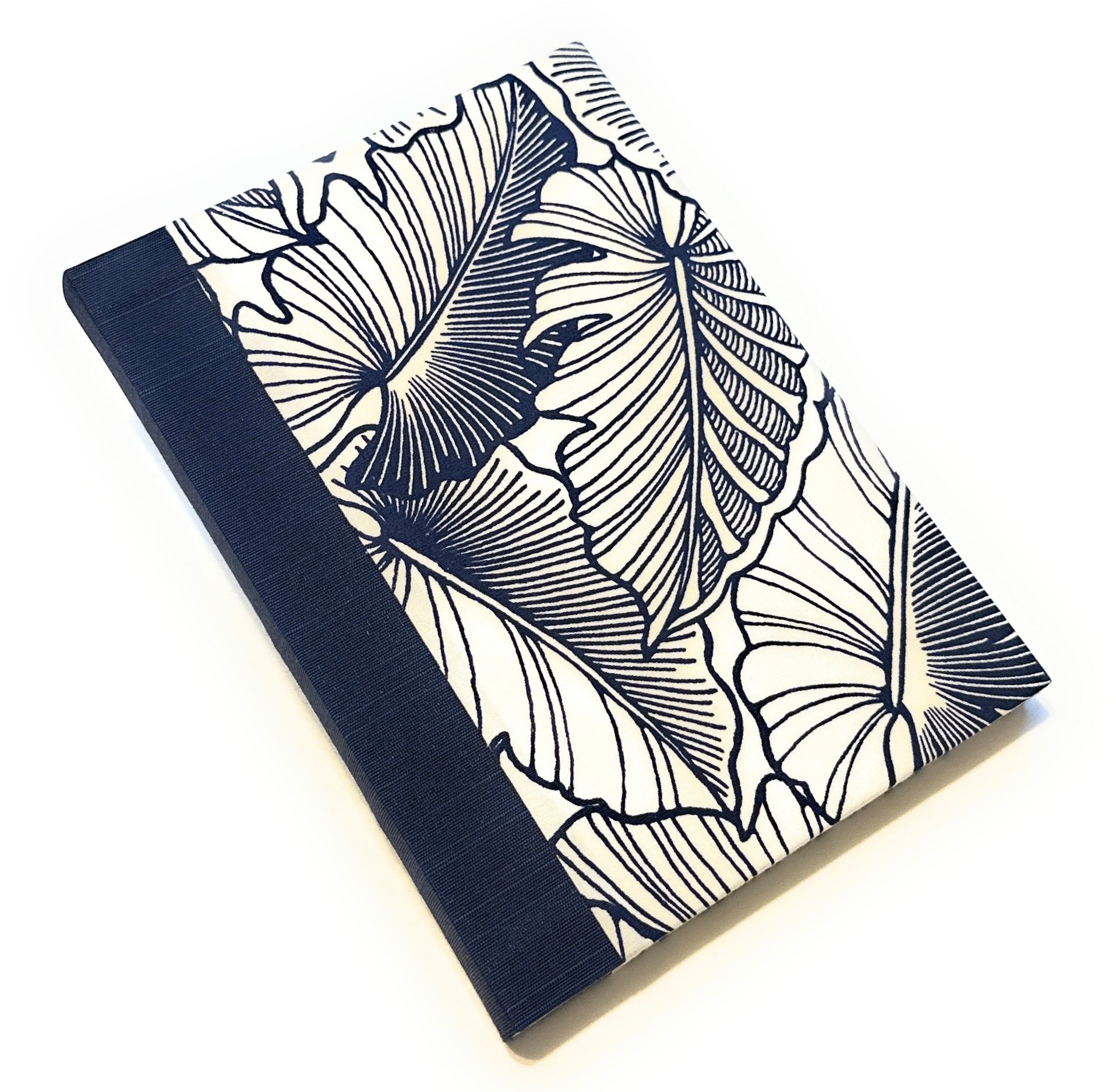 This handmade journal showcases a striking navy blue and white botanical leaf pattern on a high-quality fabric cover. The deep navy bookcloth spine complements the intricate tropical leaf design, creating a sophisticated yet nature-inspired look. Designed for writing, journaling, or sketching, this artisan notebook is crafted with durable materials, making it a perfect gift for writers, artists, and stationery lovers.