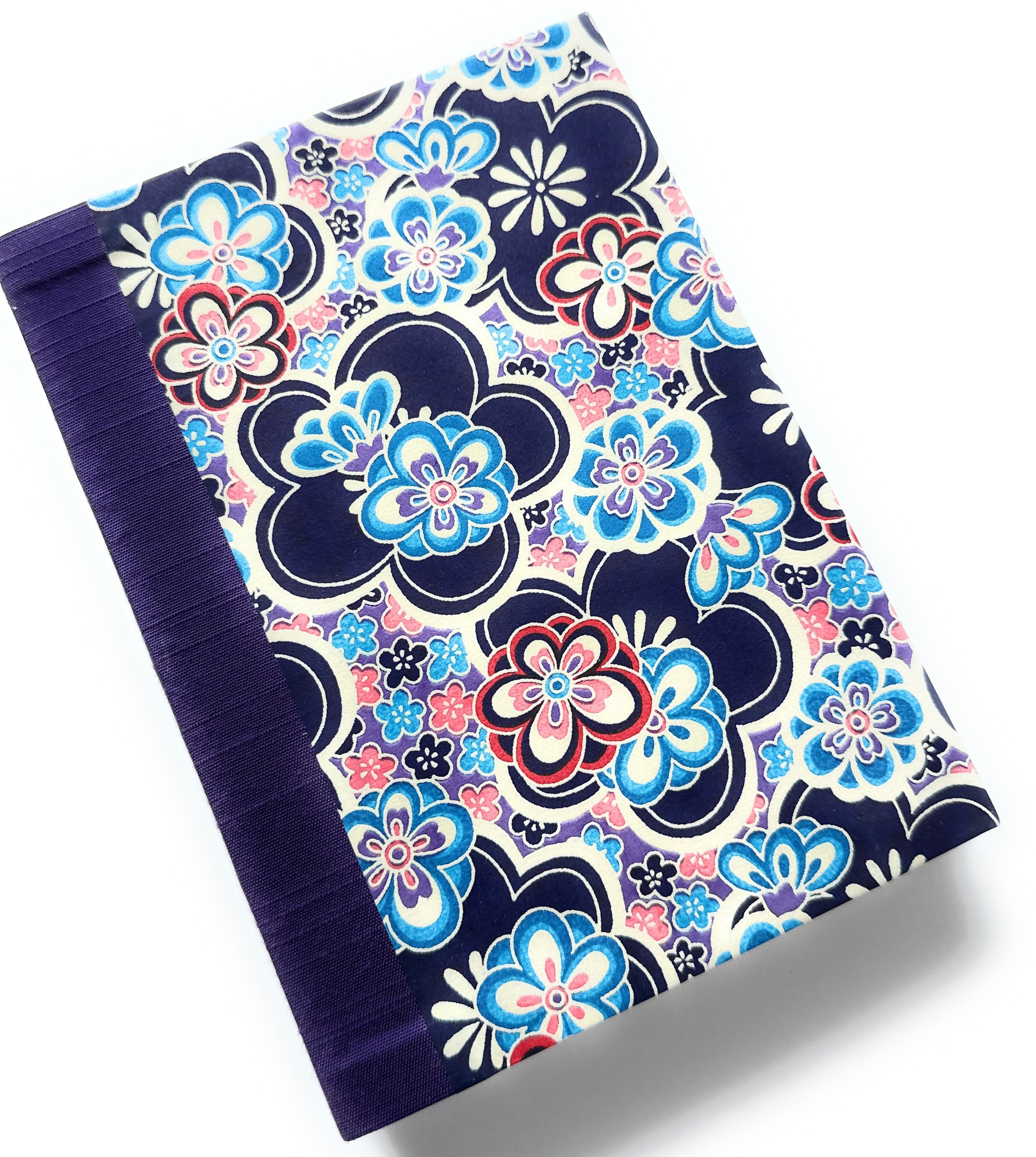 This handcrafted journal features a striking blue, red, and pink floral pattern on a dark navy background, complemented by a deep purple book cloth spine. Designed for writing, journaling, or sketching, this high-quality notebook is both durable and stylish. A perfect gift for writers, artists, and stationery lovers, this unique journal blends traditional craftsmanship with modern design.
