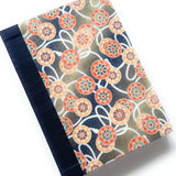 This handcrafted journal features an intricate Japanese cartwheel pattern in warm orange, red, and blue tones, set against a beige backdrop. A sturdy navy book cloth spine adds durability and elegance, making this notebook ideal for journaling, note-taking, or creative writing. Inspired by traditional Japanese textiles, this unique handmade journal is a perfect gift for writers, artists, and stationery lovers.