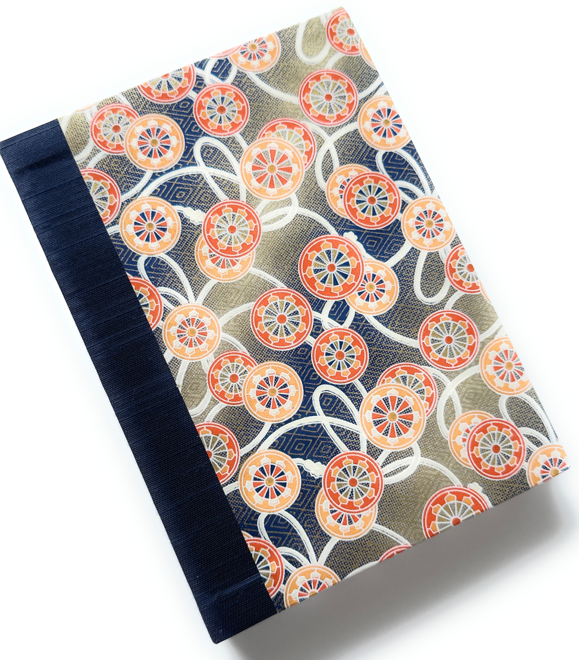 This handcrafted journal features an intricate Japanese cartwheel pattern in warm orange, red, and blue tones, set against a beige backdrop. A sturdy navy book cloth spine adds durability and elegance, making this notebook ideal for journaling, note-taking, or creative writing. Inspired by traditional Japanese textiles, this unique handmade journal is a perfect gift for writers, artists, and stationery lovers.