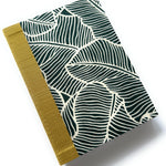 This handcrafted fabric journal features a bold jungle leaf pattern in deep green and cream, inspired by tropical foliage. The gold book cloth spine adds a sophisticated contrast, making it a stylish and durable choice for journaling, note-taking, or sketching. Perfect for writers, artists, and stationery enthusiasts, this unique fabric-covered notebook combines elegance with functionality.