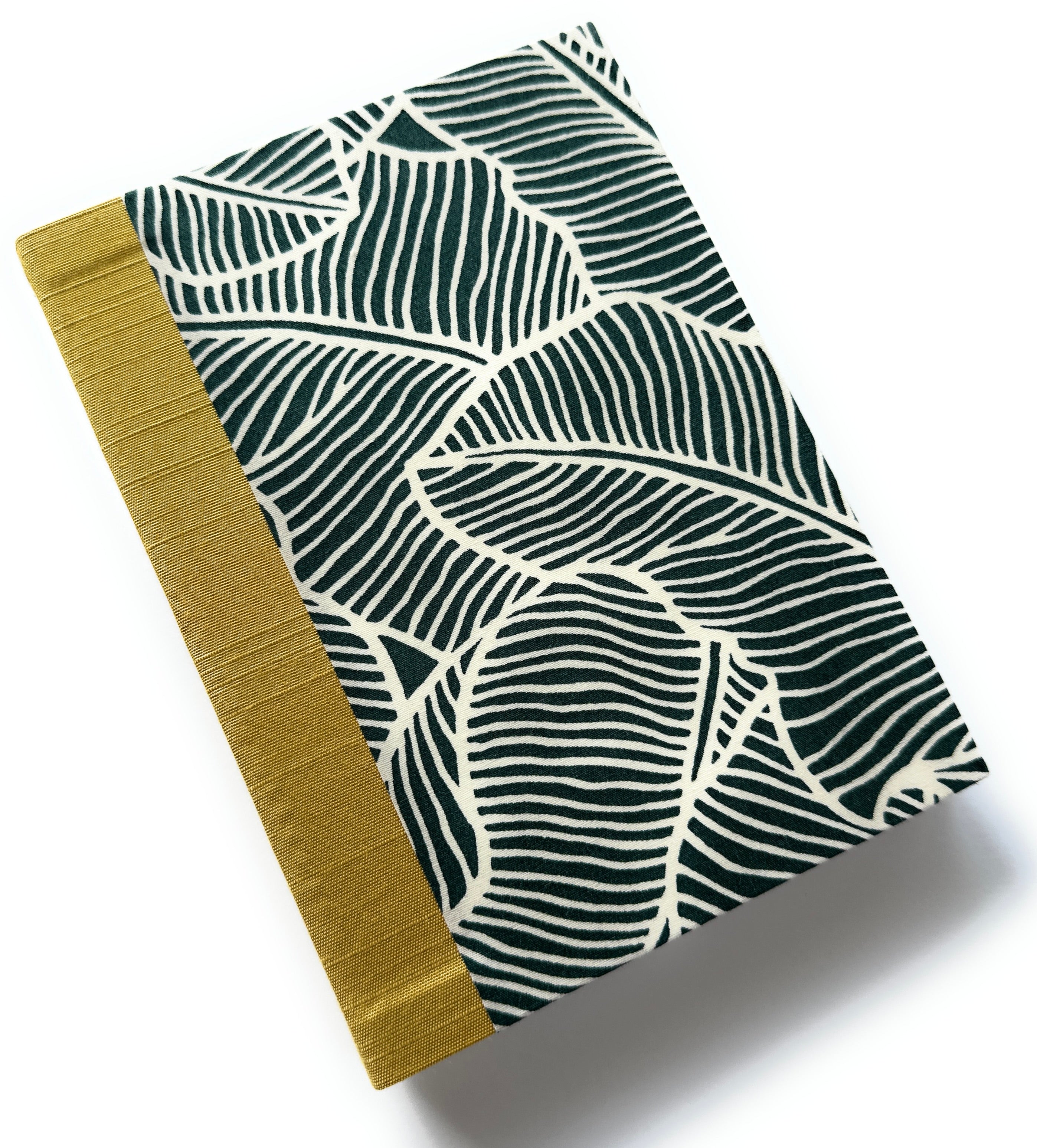 This handcrafted fabric journal features a bold jungle leaf pattern in deep green and cream, inspired by tropical foliage. The gold book cloth spine adds a sophisticated contrast, making it a stylish and durable choice for journaling, note-taking, or sketching. Perfect for writers, artists, and stationery enthusiasts, this unique fabric-covered notebook combines elegance with functionality.