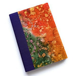 The Chikyū keepsake card showcases a vibrant, earth-inspired design with a rich blend of fiery oranges, deep greens, and golden accents, resembling natural mineral formations. The deep purple book cloth spine adds an elegant contrast, making this a unique and artistic piece for preserving heartfelt messages and special memories.