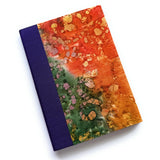The Chikyū keepsake card showcases a vibrant, earth-inspired design with a rich blend of fiery oranges, deep greens, and golden accents, resembling natural mineral formations. The deep purple book cloth spine adds an elegant contrast, making this a unique and artistic piece for preserving heartfelt messages and special memories.