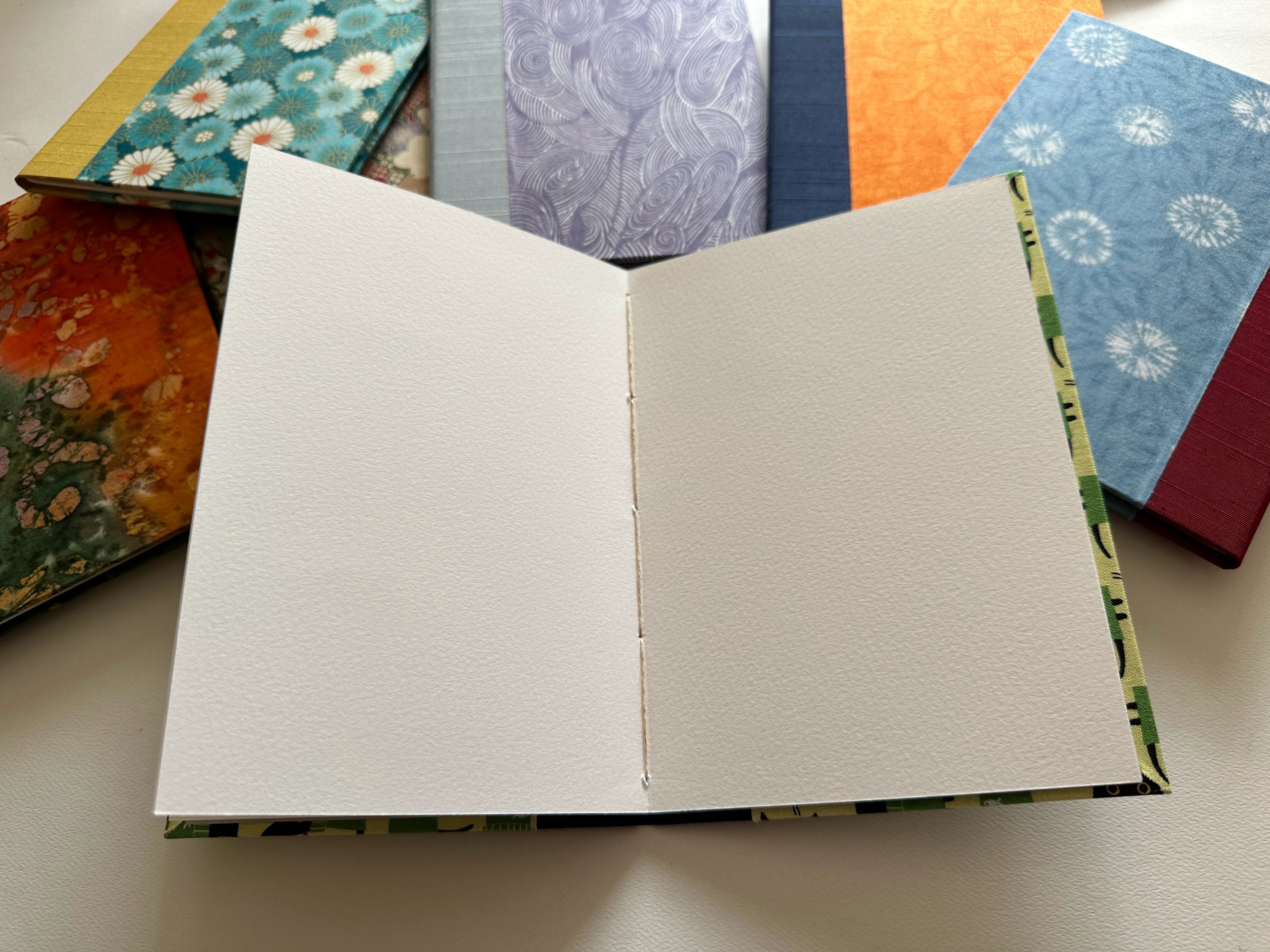 An open handmade keepsake card showcasing high-quality textured blank pages, ideal for heartfelt messages, signatures, or special notes. The fabric-covered hardcover adds elegance, while the surrounding designs highlight the variety of available styles.