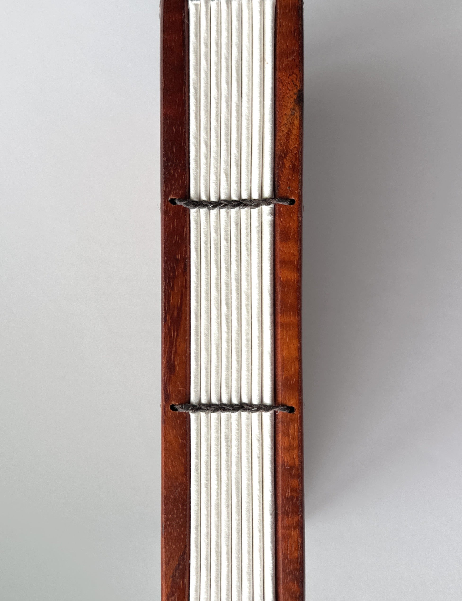 Close-up view of the exposed spine of a handcrafted Koa wood Coptic journal, showcasing the intricate hand-stitched binding with dark thread. The open-spine design allows for a flexible and durable structure, making it ideal for writing or sketching.