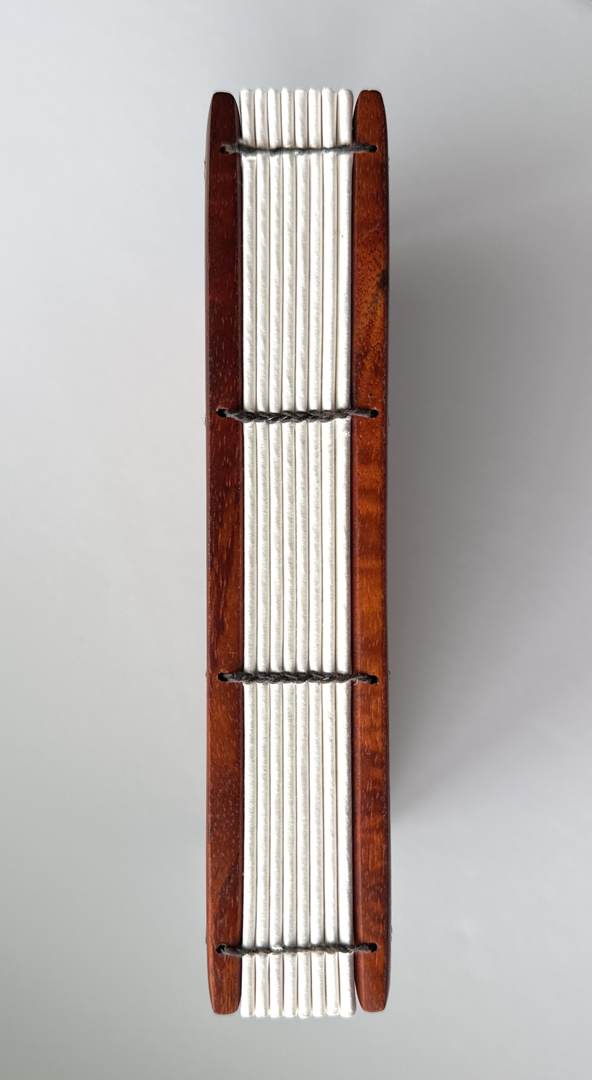 Close-up view of the exposed spine of a handcrafted Koa wood Coptic journal, showcasing the intricate hand-stitched binding with dark thread. The open-spine design allows for a flexible and durable structure, making it ideal for writing or sketching.