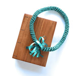 Handmade Lychee wood Coptic journal paired with a teal Hawaiian ribbon lei. The wooden cover has a smooth, natural grain, and the journal lays flat when open.