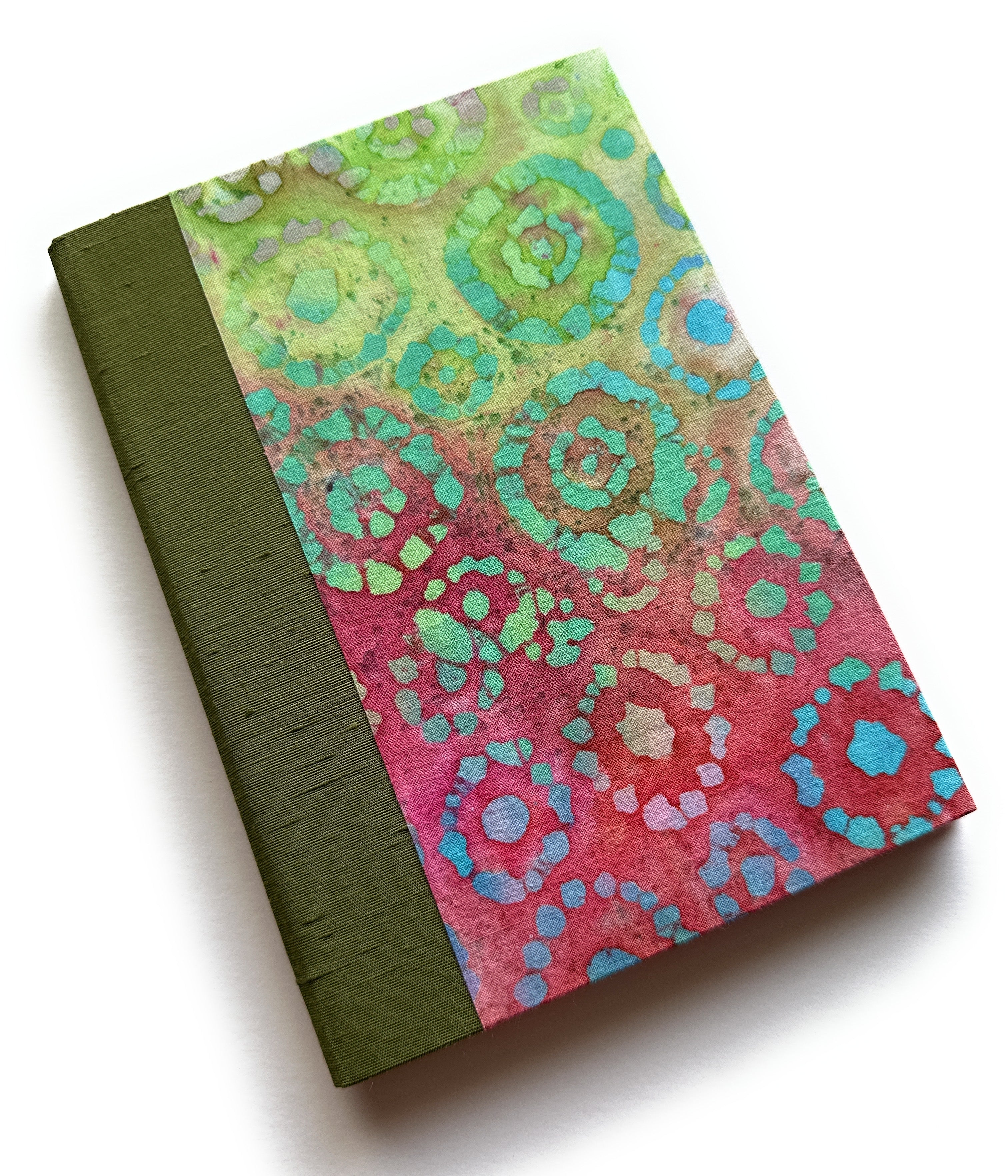 A handbound card featuring vibrant circular batik patterns in pink, green, and aqua hues, with an olive green cloth spine - designed as a keepsake card