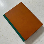 Brown leather journal with green leather spine on a speckled surface