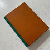 Brown leather journal with green leather spine on a speckled surface