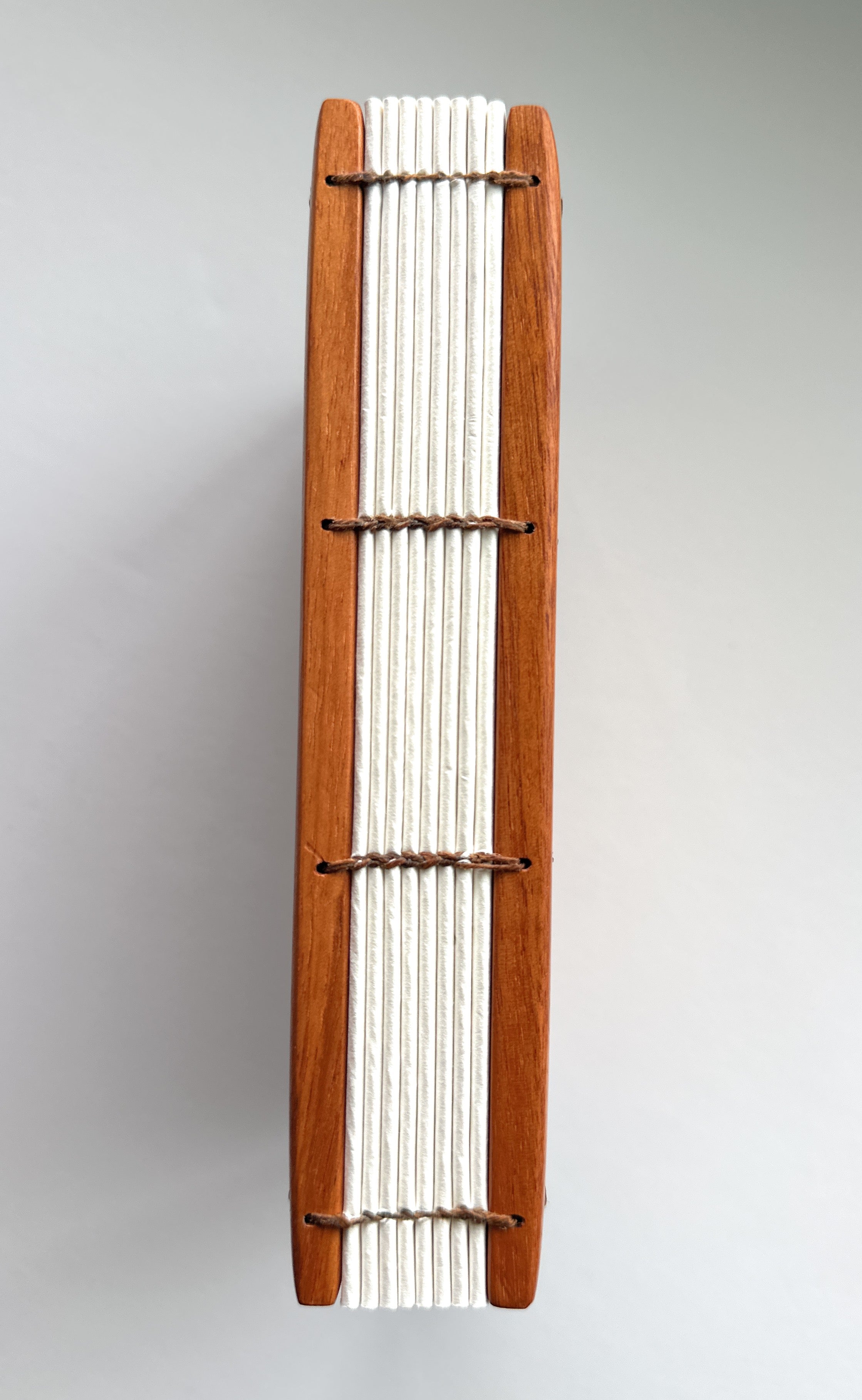A close-up view of a handmade Lychee wood Coptic journal, showcasing its beautifully exposed Coptic stitch along the spine. The durable wooden covers frame the high-quality, cream-colored pages, bound together with natural waxed thread for flexibility and strength. This binding style allows the journal to lay completely flat, making it ideal for artists, writers, and journal enthusiasts who appreciate traditional bookbinding craftsmanship.