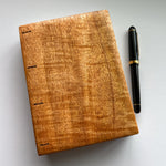 A beautifully handcrafted Mango Wood Coptic Journal with rich natural grain, placed next to a black and gold fountain pen for scale. This artisanal wooden notebook is ideal for journaling, sketching, or creative writing, blending timeless craftsmanship with functionality.