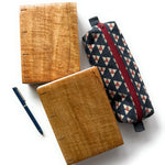 Two handcrafted Mango Wood Coptic Journals displayed alongside a patterned fabric pencil case and a navy blue fountain pen. These artisanal wooden notebooks feature exposed spines for flexibility and durability, making them perfect for journaling, sketching, or note-taking. A stylish and functional set for writers, artists, and creatives who appreciate craftsmanship and natural materials.