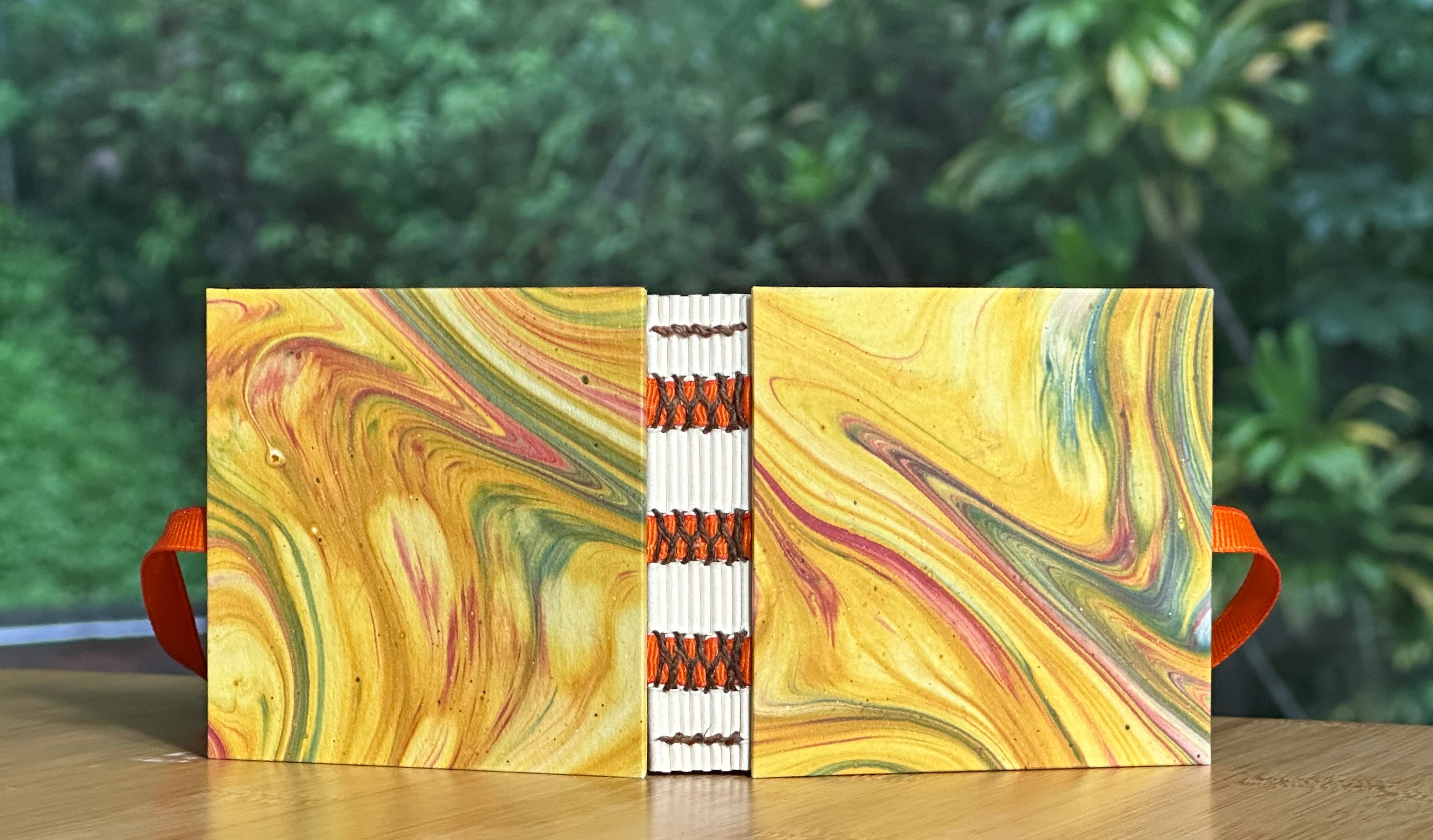 Colorful marbled miniature notebook with orange accents on a wooden surface
