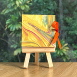 Marble-patterned miniature book on a wooden easel with an orange ribbon against a blurred green foliage background