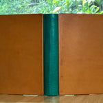 A leather-bound book with a green spine on a wooden surface with a blurred natural background