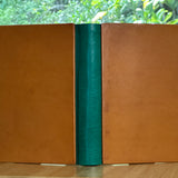 A leather-bound book with a green spine on a wooden surface with a blurred natural background