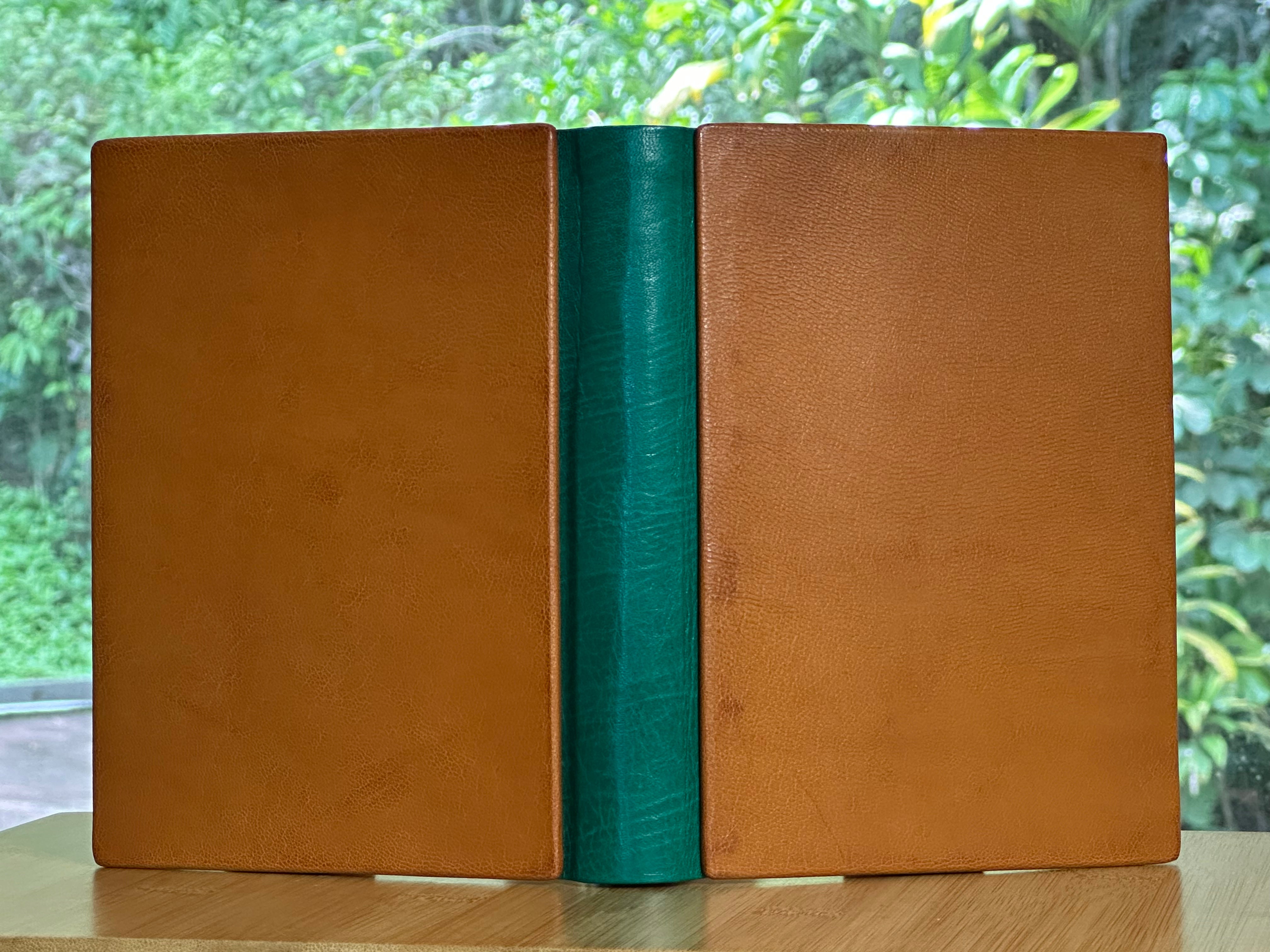 A leather-bound book with a green spine on a wooden surface with a blurred natural background