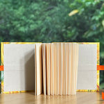 Open miniature book with orange ribbon on a wooden surface with a green blurred background