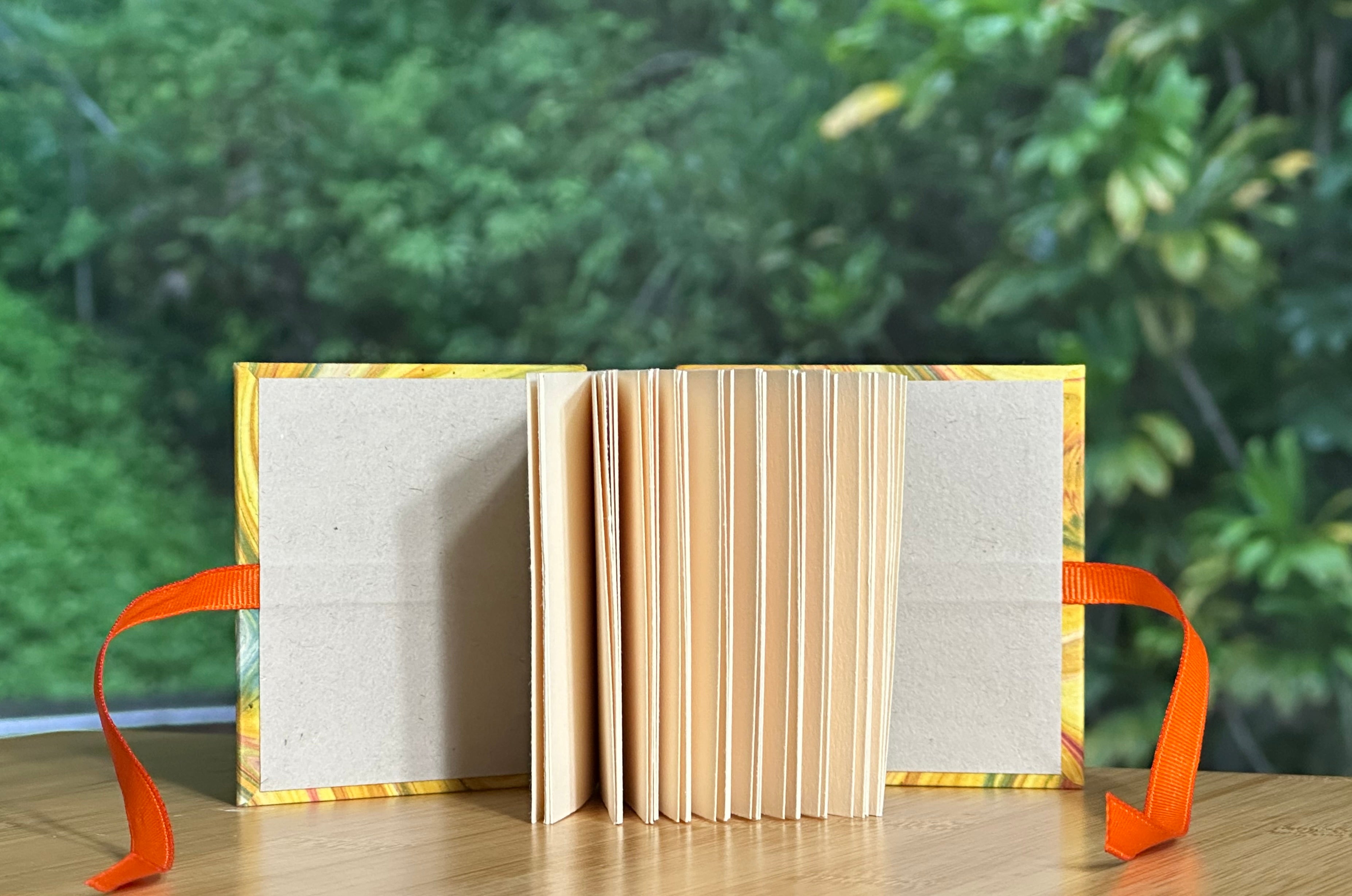 Open miniature book with orange ribbon on a wooden surface with a green blurred background