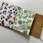 Open notebook with Mickey Mouse pattern on one page and floral pattern on the other, on a speckled surface.