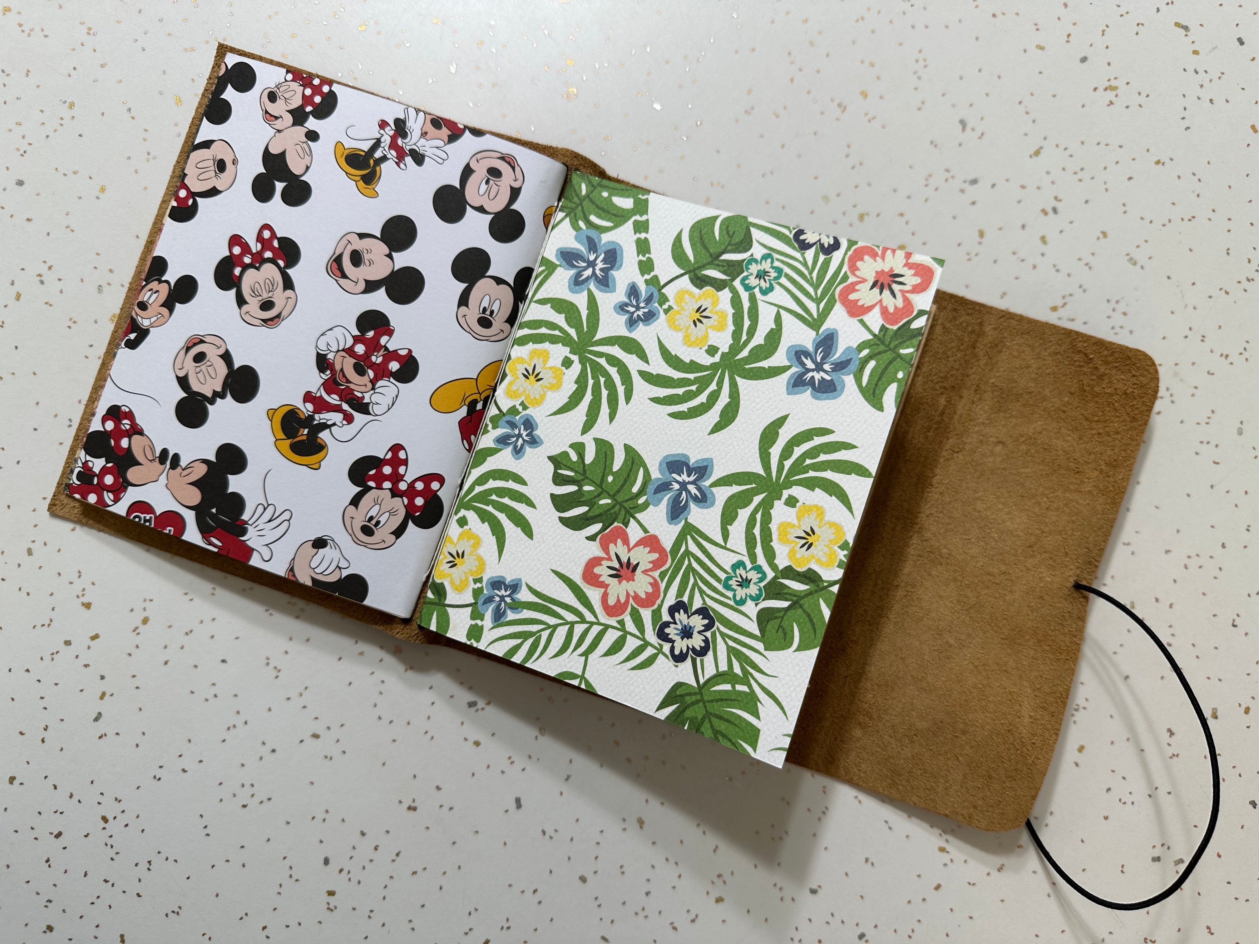 Open notebook with Mickey Mouse pattern on one page and floral pattern on the other, on a speckled surface.