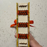 Hand holding a small, intricately miniature bound book so the spine is visable.